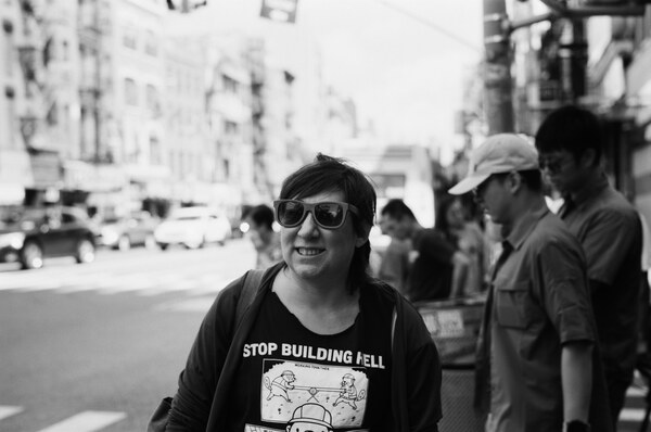 Woman in sunglasses and black shirt that reads 'stop building hell'